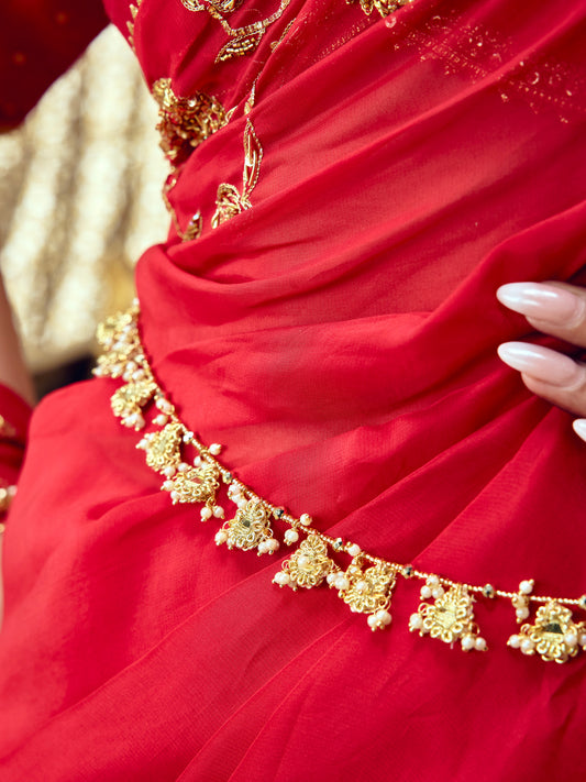 Jhilmil gold-toned waist belt with ornate motifs and delicate bead drops styled over a red saree